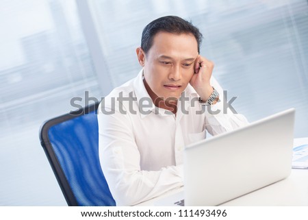 Tired businessman sitting at the table and looking at laptop at office