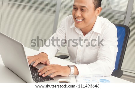 Happy office worker sitting at the table and working with laptop