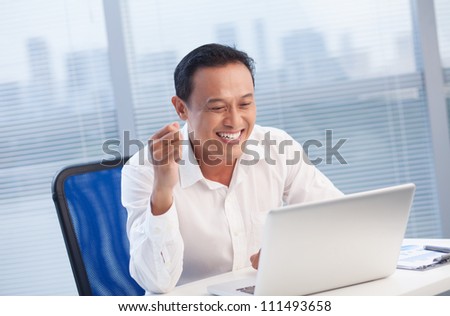 Happy office worker looking with excitement at laptop at office