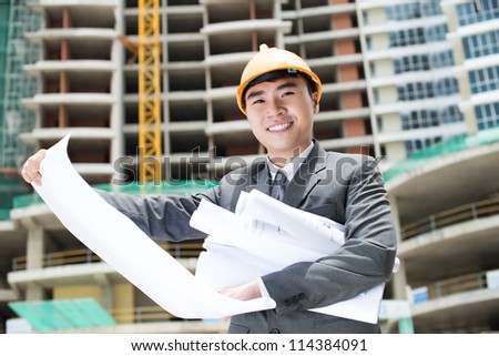 Portrait of a cheerful engineer studying blueprints on site