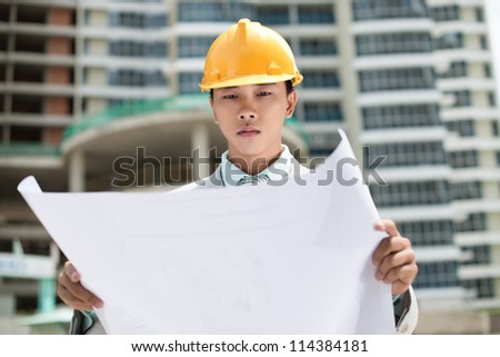 Serious young man in hardhat studying blueprint