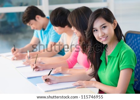 Row of students sitting in classroom and writing