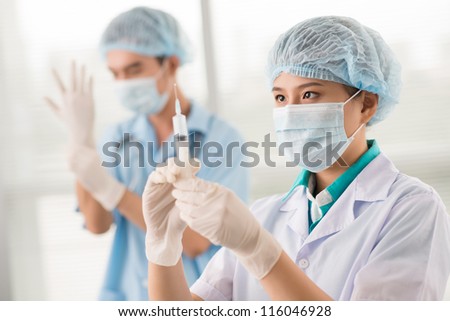 Nurse filling the syringe while male doctor getting ready for a medical procedure