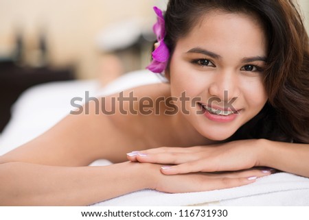Beautiful spa girl with a flower in her hair looking at camera with a smile
