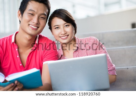 Image of joyful college students getting knowledge from different sources Ã?Â¢?? a book and a laptop