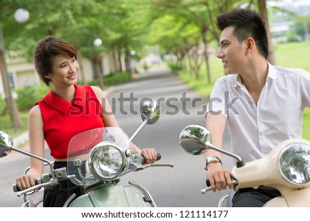 Young couple riding scooters in park and smiling to each other