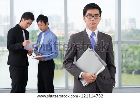 Portrait of a young business leader holding a pile of office folders