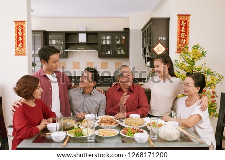 Big Vietnamse family enjoying traditional dinner and celebrating Lunar New Year, couplets with best wishes for coming year in the background