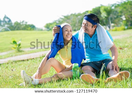 Senior couple after sports activities sitting on the grass in the park