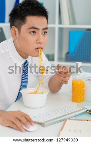 Vertical image of a diligent worker eating noodles without leaving office