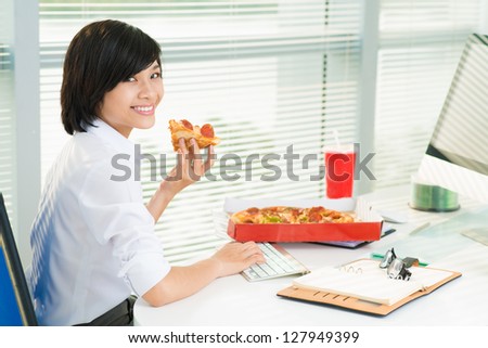 Smiling office lady working at lunchtime and eating pepperoni