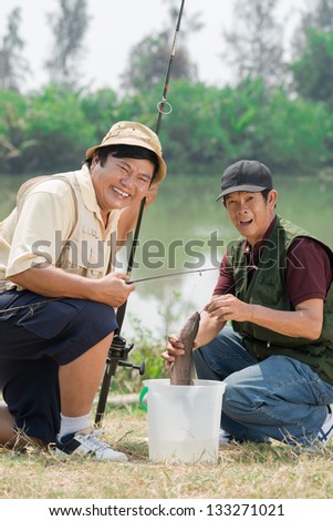 Portrait of smiling fishers holding fish and looking at camera