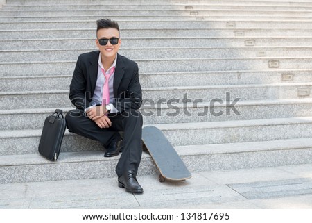 Portrait of a happy manager with skateboard sitting on stairs outdoors