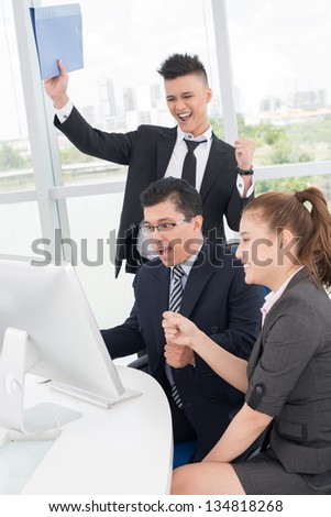 Vertical image of excited co-workers sitting in front of the computer