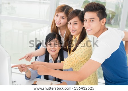 Portrait of cheerful students and their tutor pointing at the computer screen