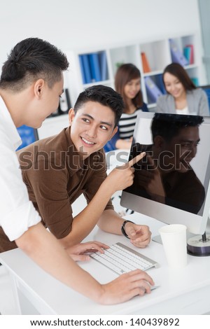 Vertical image of co-workers standing in front of the computer on the foreground