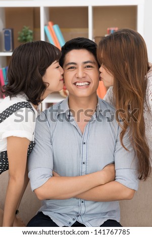 Vertical portrait of a young man looking at camera, girls kissing him inside