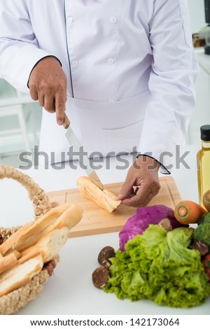 Vertical image of a chef cook\'??s hands cutting bread in the kitchen