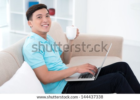 Happy man working from home sitting on a comfortable sofa and sipping tea