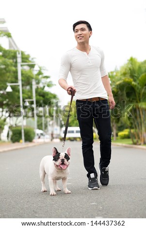 Vertical image of a smiling young man walking his pet