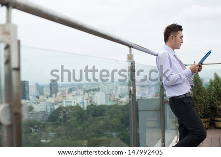 Profile image of a young businessman standing with a gadget during the break outside