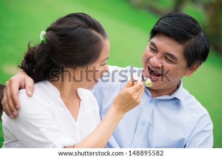 Close-up image of a mature couple, a woman feeding his man on the foreground