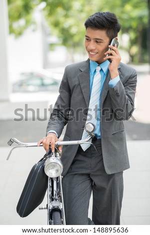 Vertical image of a businessman talking by phone and riding a bicycle on the way at work