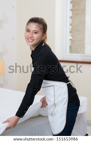 Vertical portrait of a cleaning lady making a bed in the apartment