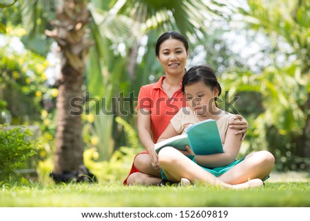 Copy-spaced image of a mother teaching her daughter to read outside