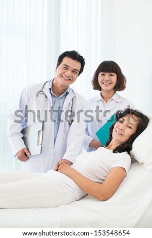 Vertical portrait of a happy doctor with a nurse standing near a patient\'s bed in the hospital
