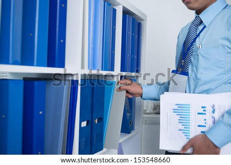 Cropped image of a businessperson taking a folder with documents from the archive on the foreground
