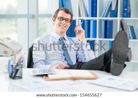 Portrait of a relaxed businessman with legs on the table smiling and looking at camera on the foreground