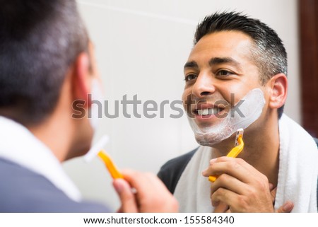 Close-up image of a shaving man looking in the mirror and smiling on the foreground
