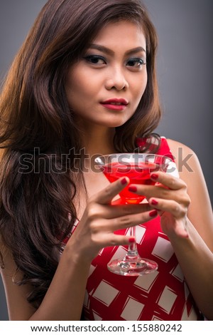 Vertical portrait of a charming lady in red with a glass of cocktail against a grey background