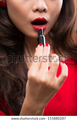 Vertical image of a vogue young woman applying red lipstick on the foreground