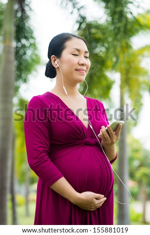 Vertical image of a pregnant woman listening to the classical music with her baby in belly outside