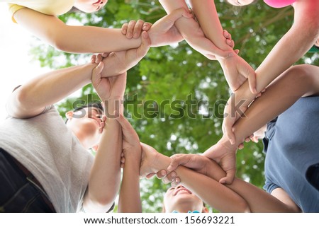 Close-up of hands of young adults joined in a circle on the foreground