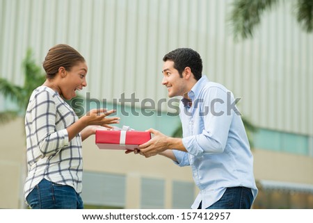Copy-spaced image of an excited couple where a boyfriend presenting his girlfriend with a giftbox on the foreground