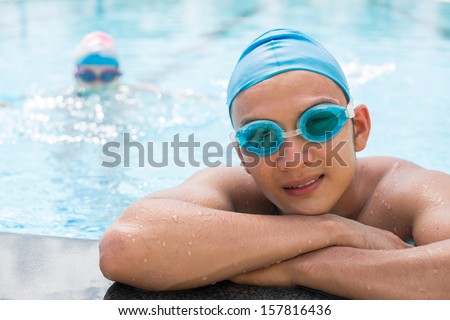Close-up portrait of a young swimmer in protective goggles leaning on the pool and posing at camera on the foreground