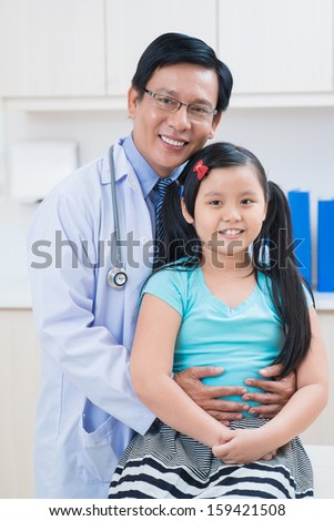 Vertical portrait of a doctor with his little patient smiling and looking at camera in the clinic