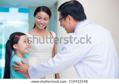 Image of a pediatrician having an appointment with a little child and her mom on the foreground