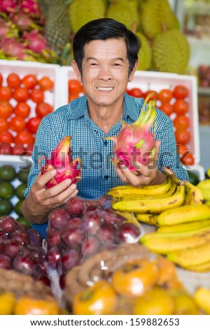 Vertical portrait of a cheerful husband with fruits in hands in the market on the foreground