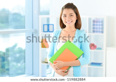 Copy-spaced portrait of a young student with copybooks smiling and looking at camera on the foreground