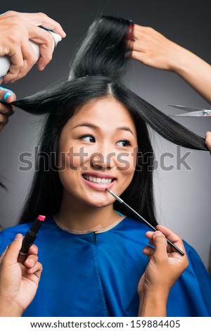 Vertical image of a young woman preparing for something by her professional stylists over grey