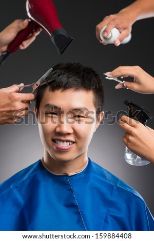 Cropped image of stylists doing professional haircut for a young man against a grey background