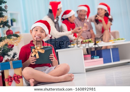 Portrait of happy family members in Santa caps interacting on Christmas evening, little boy with gift sitting in front