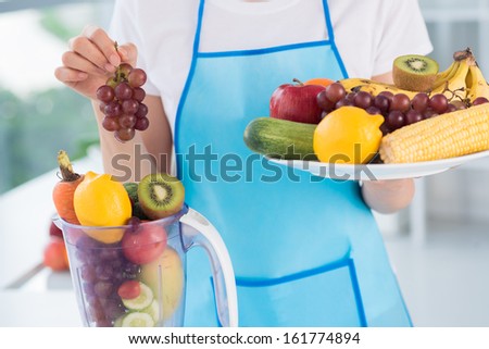 Close-up of a female cook with a plate and a food processor full of fruits and vegetables