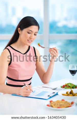 Vertical image of a young businesswoman working while her lunch inside