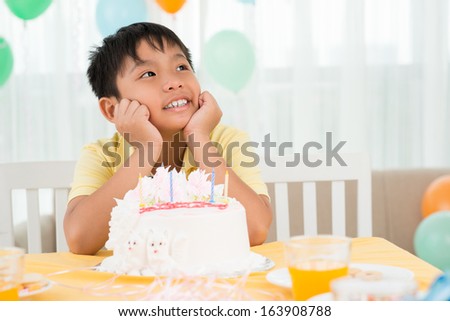Copy-spaced image of a dreaming b-day boy sitting in front of the delicious cake with candles
