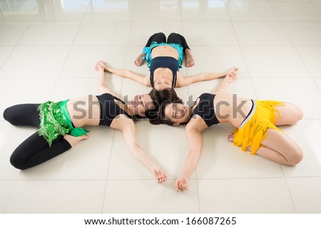 Angle view of young belly dancers lying on the floor in the star pose and looking at camera